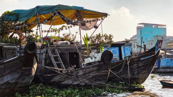 Wooden boats moored on a river, with one boat covered by a tarp and used as a floating home with plants and household items.